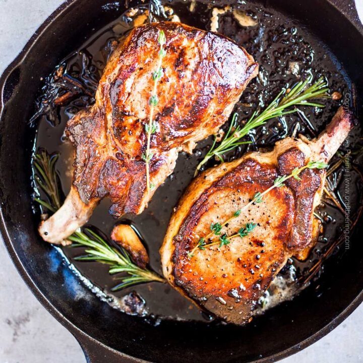 Thick pork chops in cast iron skillet with herbs and garlic.