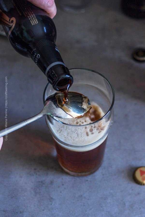 Guinness Draught stout poured over the back of a spoon to create a Black and Tan beer.