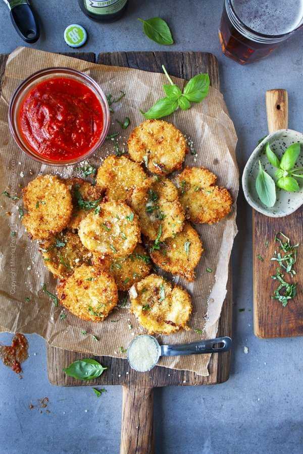 Fried mozzarella cheese rounds on a serving board with marinara dip and fresh basil.