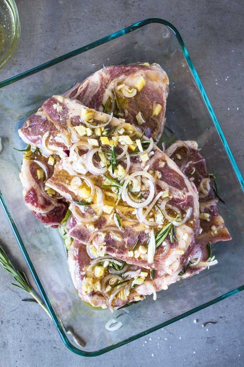 Glass container with blade lamb chops smothered in a marinade of shallots, garlic, preserved lemon rinds and juice, salt and pepper and olive oil.