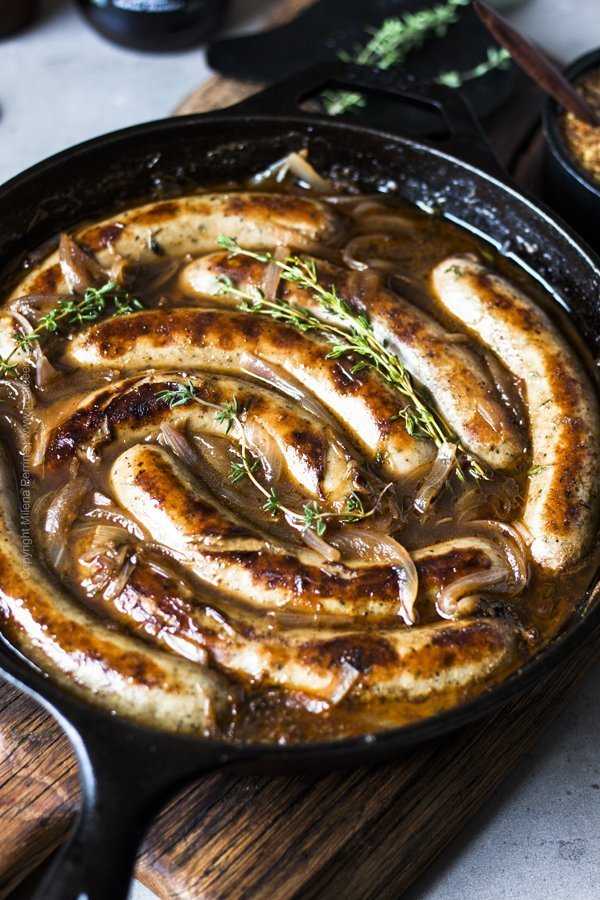 Beer braised bratwurst sausages with onions in cast iron skillet.