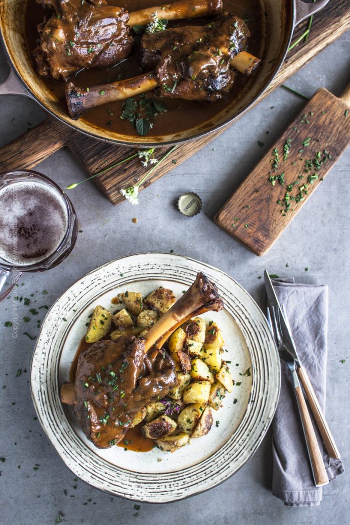 Oven braised lamb shanks - two shown in a braiser and one plated with crispy roasted potatoes.