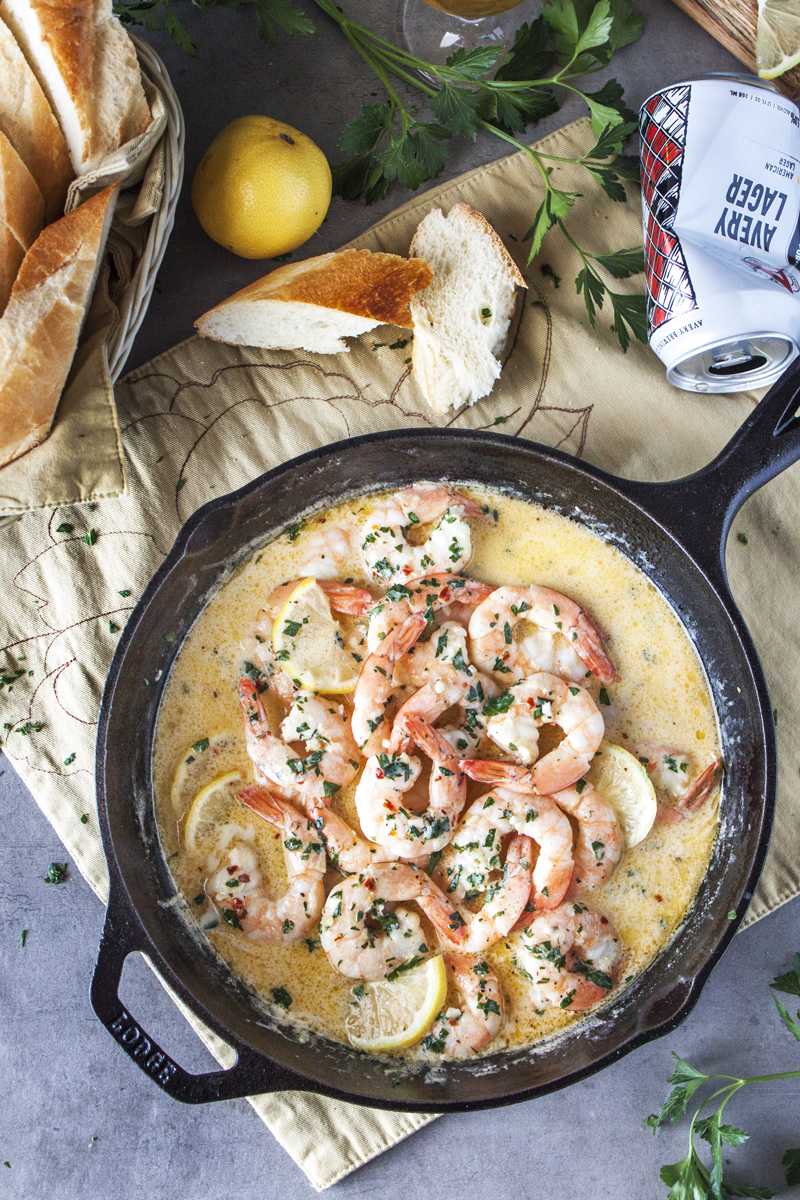 Overhead shot of scampi stylebeer shrimp skillet with baguette and parsley next to the skillet.
