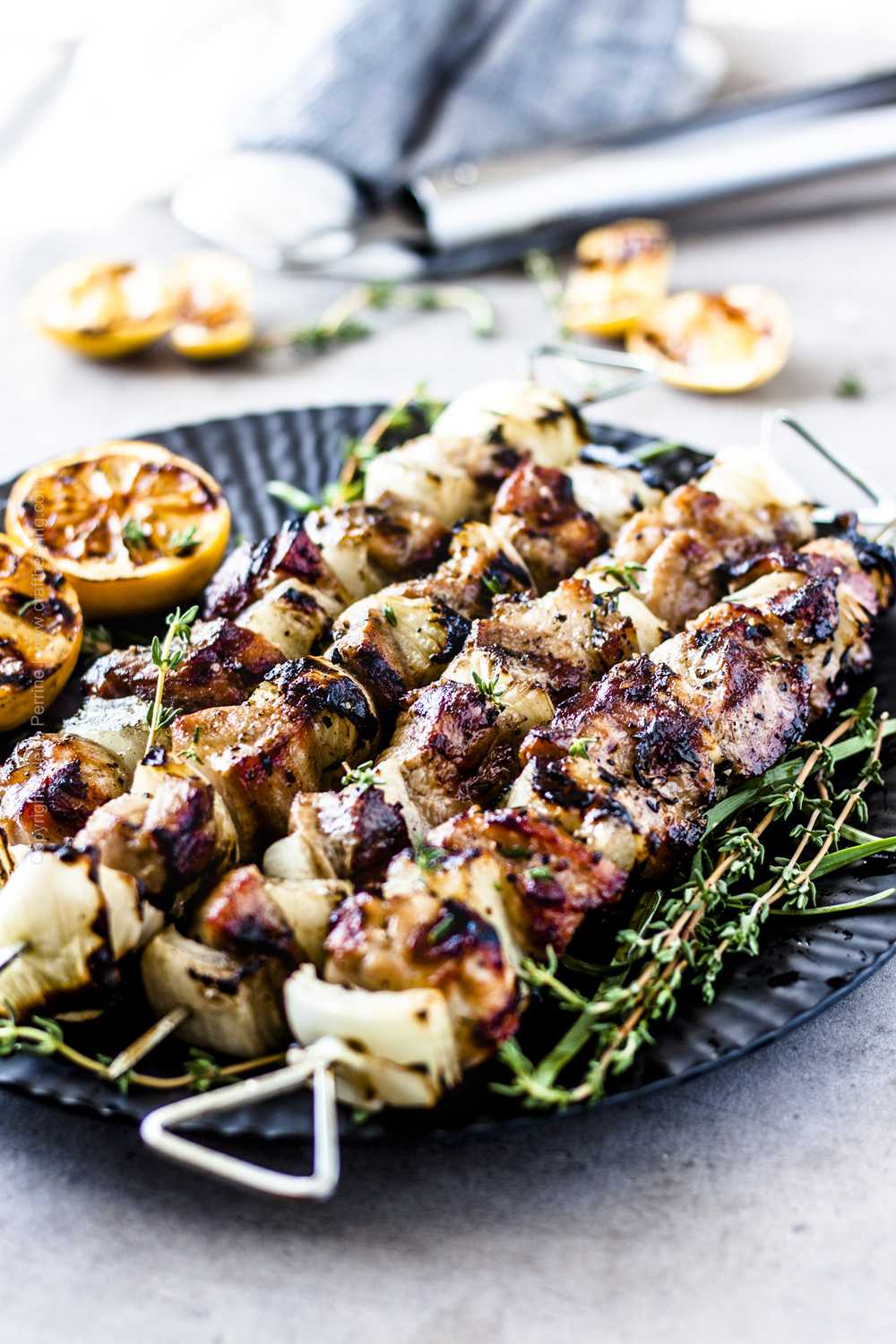 Pork kabobs in the oven, with onions and served with fresh herbs and grilled lemon halves. 
