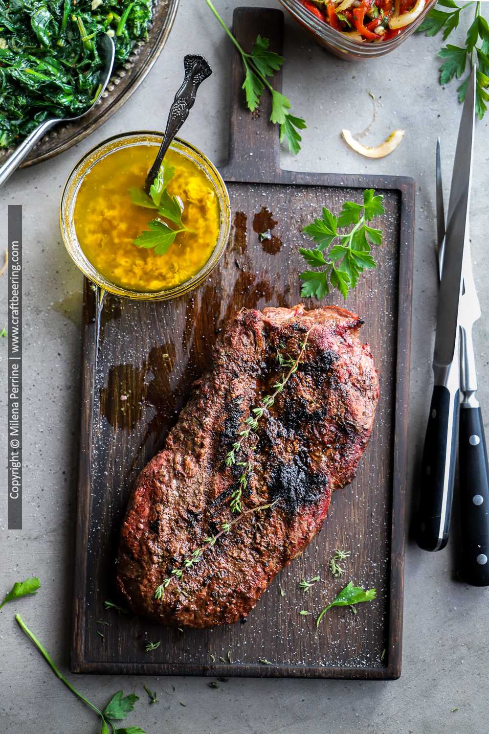 Family style flat iron steak resting on cutting board next to cowboy butter dipping sauce. 