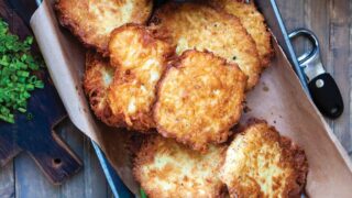 German potato pancakes known as Kartoffelpuffer are shown served in a rectangular platter with apple sauce and cured salmon sliced on the side.