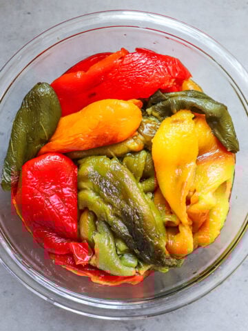 Roasted bell peppers of different colors are shown peeled and arranged in a clear glass bowl.