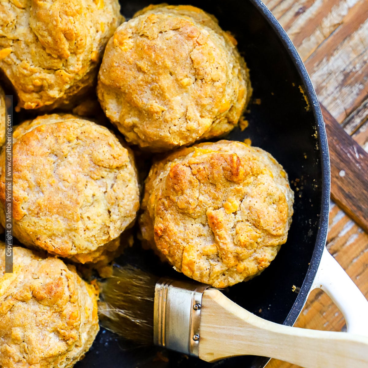 Cheddar biscuits brushed with melted butter are, hown inside cast iron pan, viewed from above.