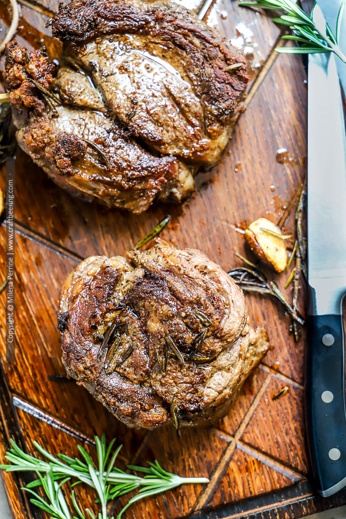 Seared chuck eye steak with rosemary and garlic is resting on a wood board.