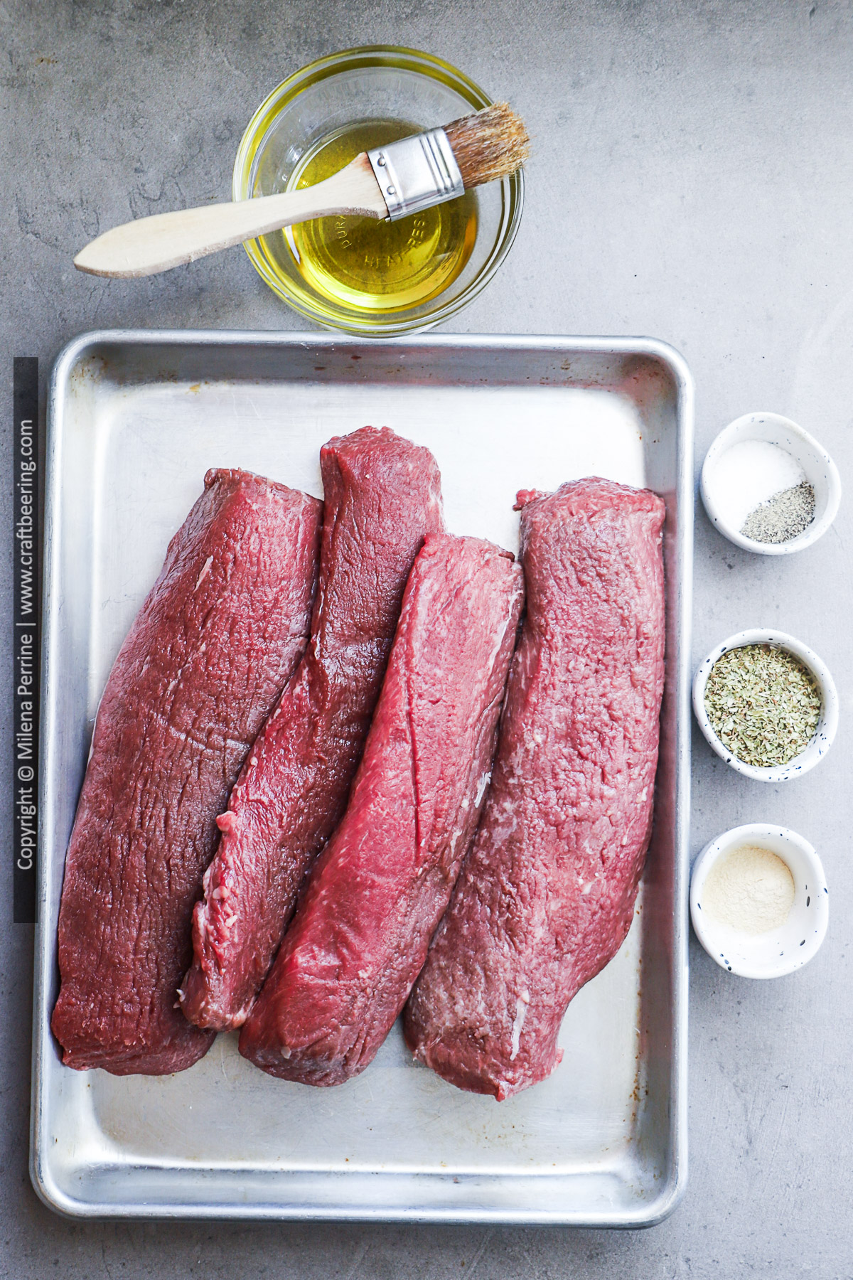 Four boneless lamb loins, raw, shown side-by-side along with ingredients for grilling. 
