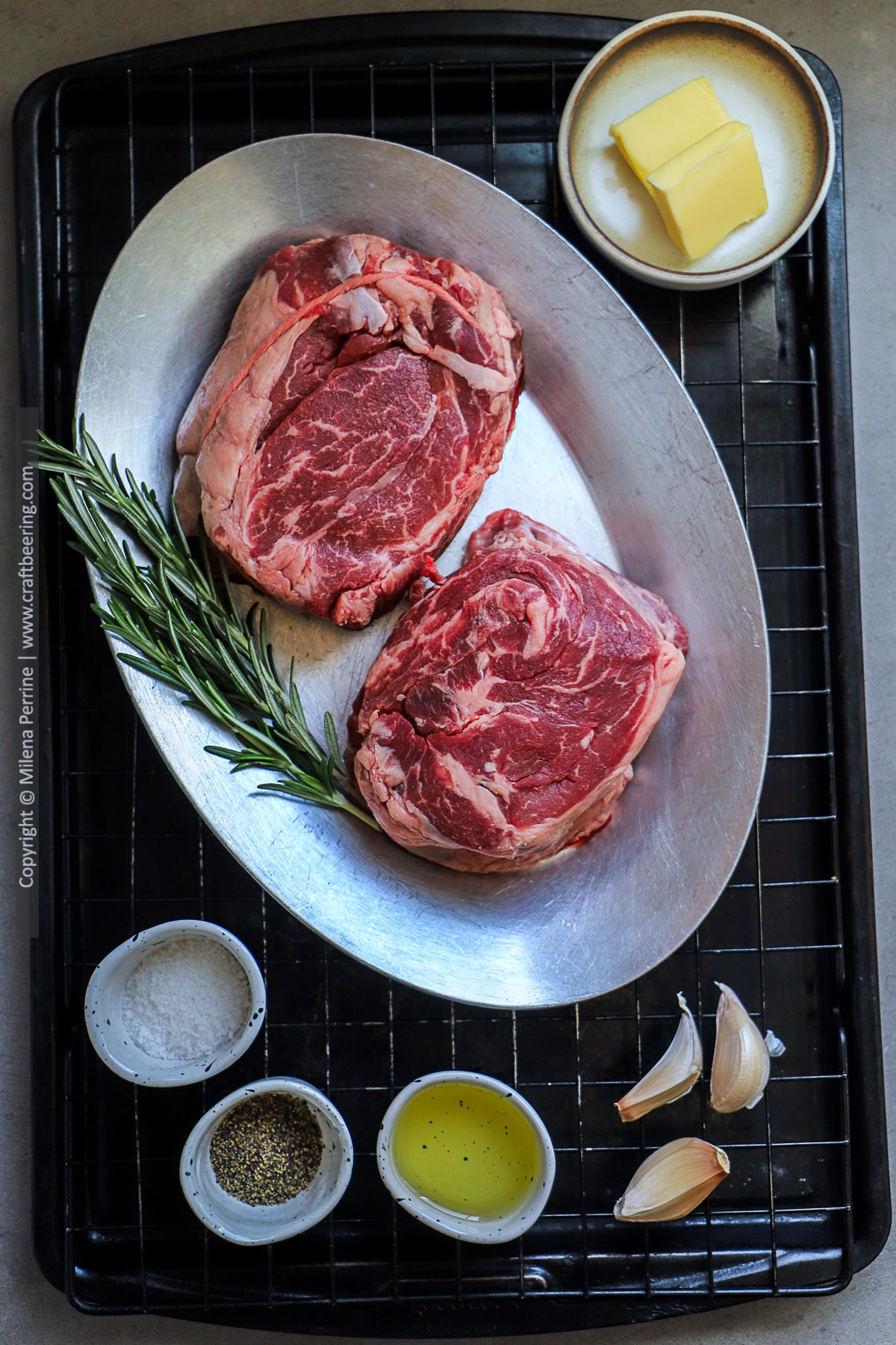 Raw chuck eye steaks are shown tied with butchers twine and next to butter, oil, rosemary, garlic and salt and pepper.