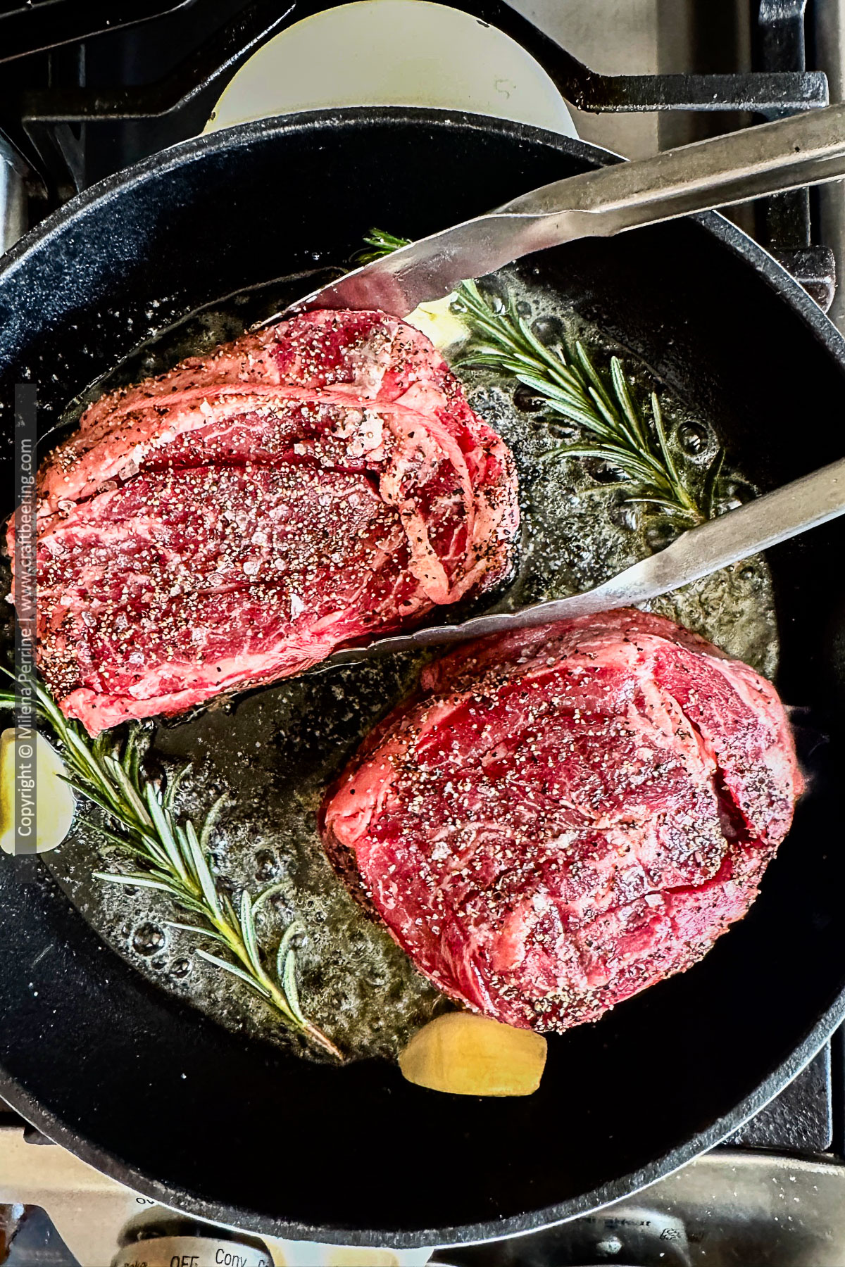Chuck eye steaks are being seared in a cast iron skillet with butter, rosemary and garlic.