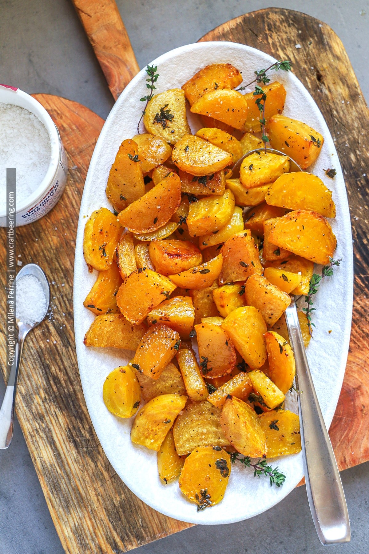 Godeln beet sliced in wedges are roasted with tyme and olve oil and shown plater in a white oval dish on top of a wood cutting board.