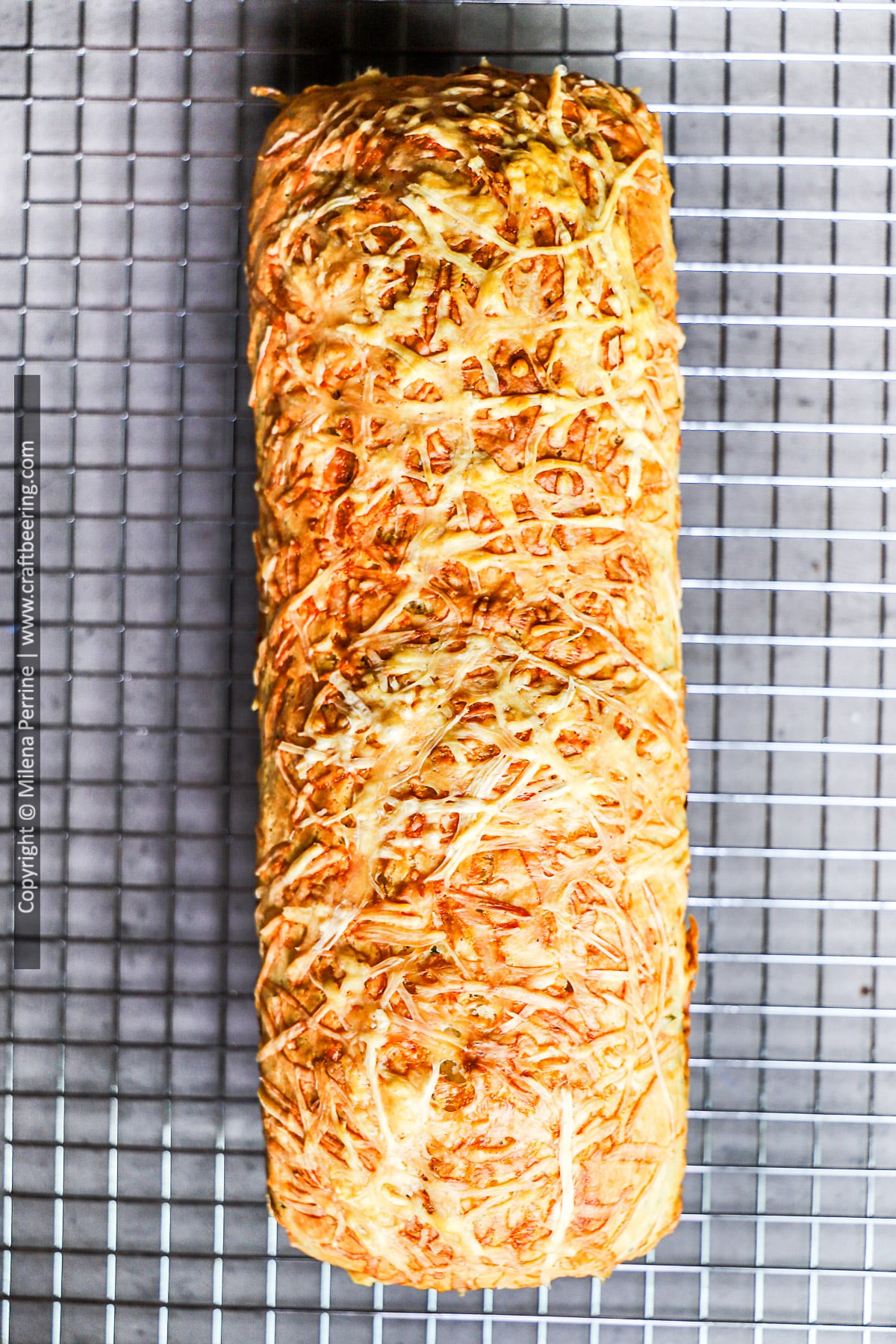 Frshly baked rosemary parmesan bread loaf without yeast is shown viewed from above cooling down over a wire rack.