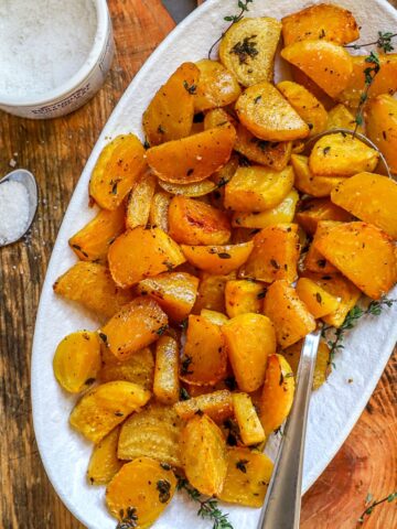 Roasted yellow beets are shown served in a white platter and garnished with thyme.
