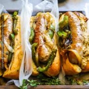 Bratwurst cooked on the stove is shown nestled in bread buns with sauteed onions and peppers and mustard.