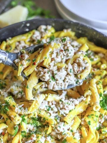 Grund chicken cream sauce pasta is shown scooped by a ladle over a pan containing the dish.