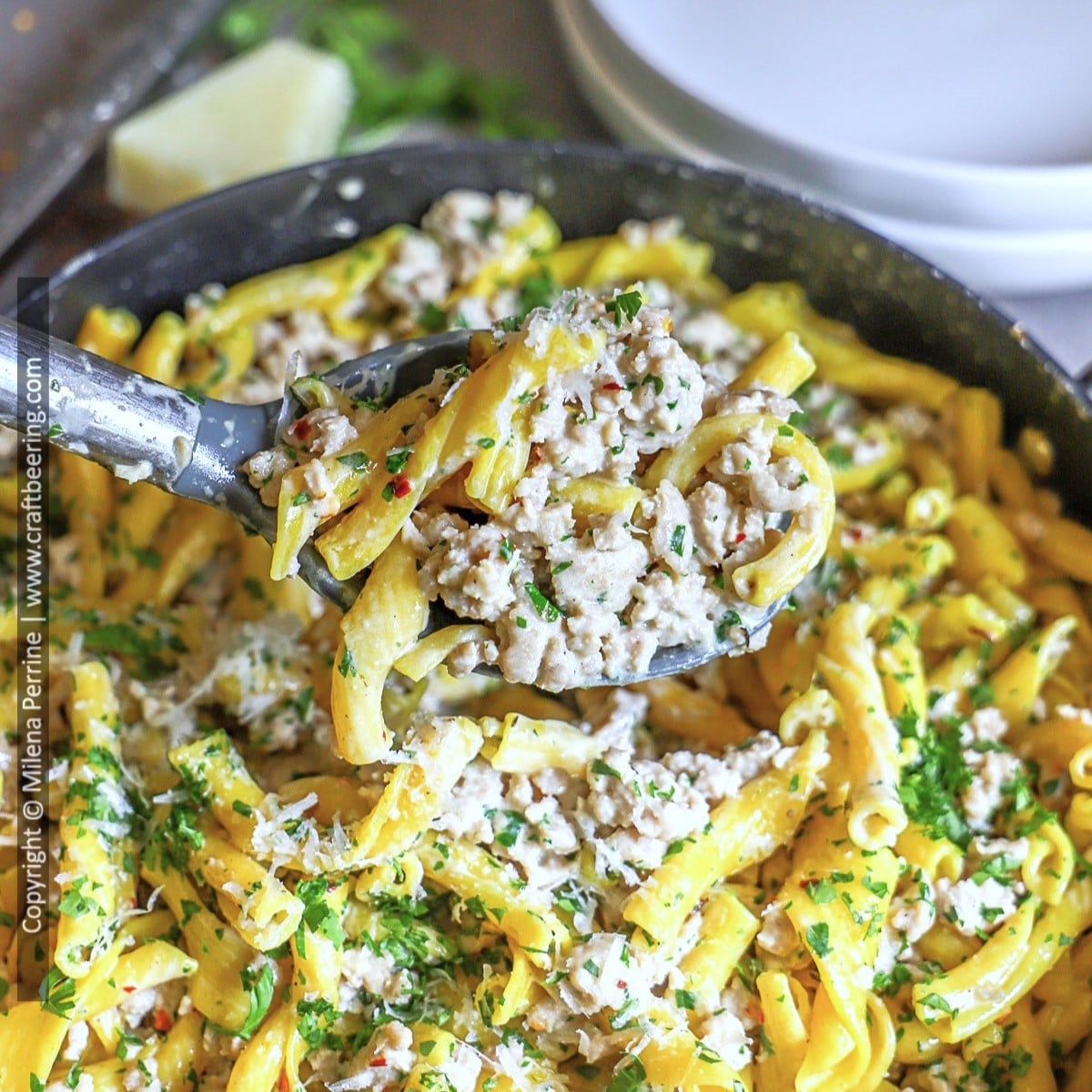 Grund chicken cream sauce pasta is shown scooped by a ladle over a pan containing the dish.