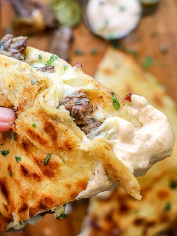 Quesadilla sauce is shown smeared over the tip of a steak quesadilla wedge held in focus.