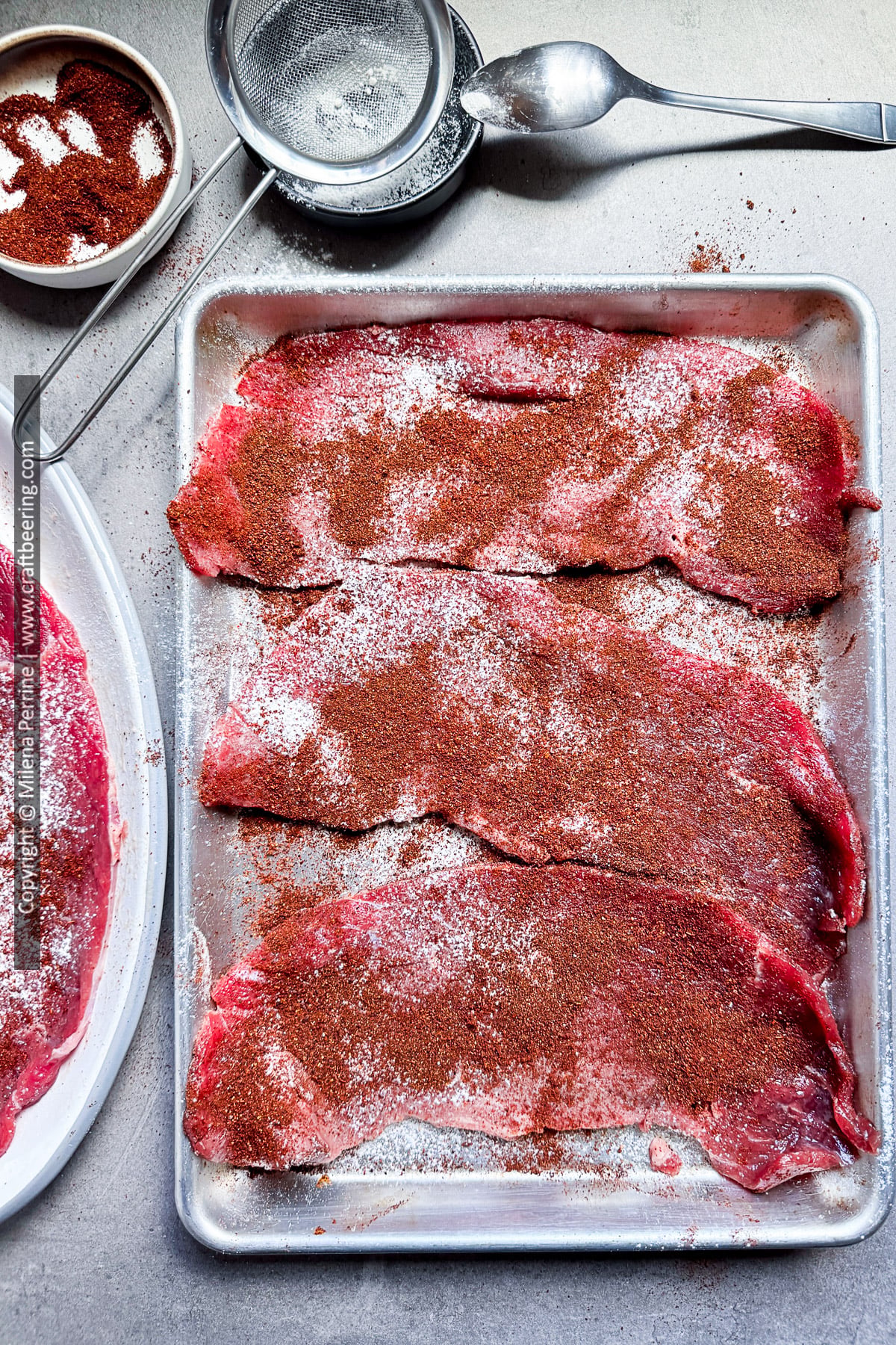 Top round steaks sliced thin as minute steak are shown dusted with flour and chili powder and ready to sear.