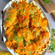 Chicken paprikash with Hungarian paprika sauce is shown viewed from above and laid over a bed of broad egg noodles garnished with parsley.