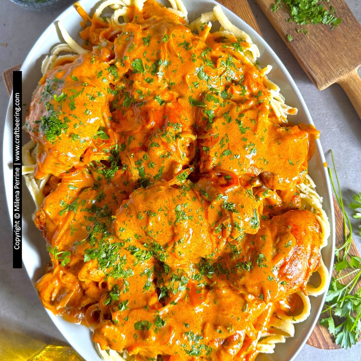 Chicken paprikash with Hungarian paprika sauce is shown viewed from above and laid over a bed of broad egg noodles garnished with parsley.