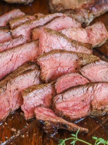 Top sirloin steak is shown sliced revealing medium-rare juicy beef cut against the grain.