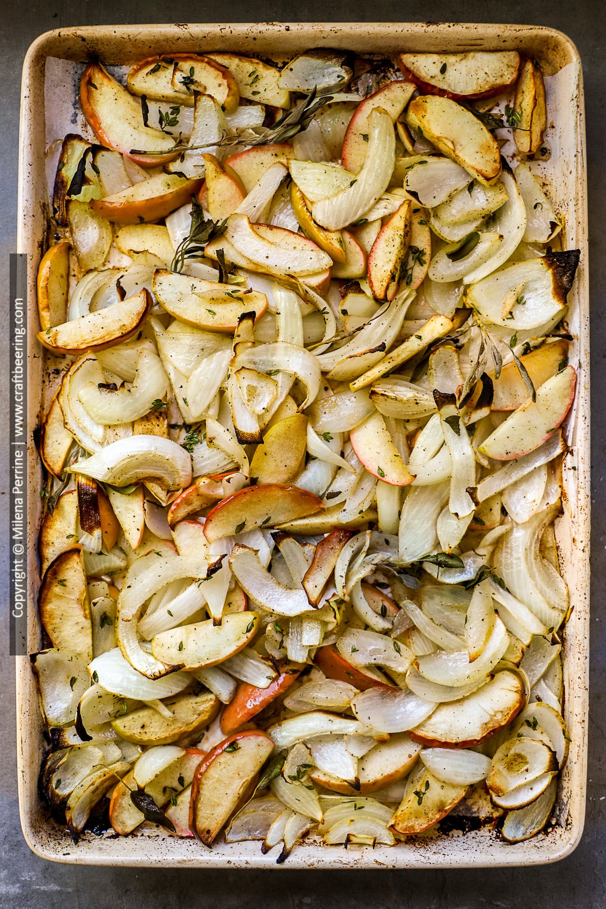 Sheet pan fried apples and onions with thyme and sage are shown still in the baking sheet, right out of the oven.