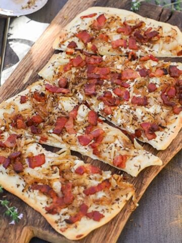 Flammkuchen German pizza with bacon and onions shown sliced onto a wooden cutting board.