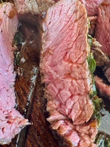 Seared top sirloin steak is shown sliced against the grain revealing tender beef.